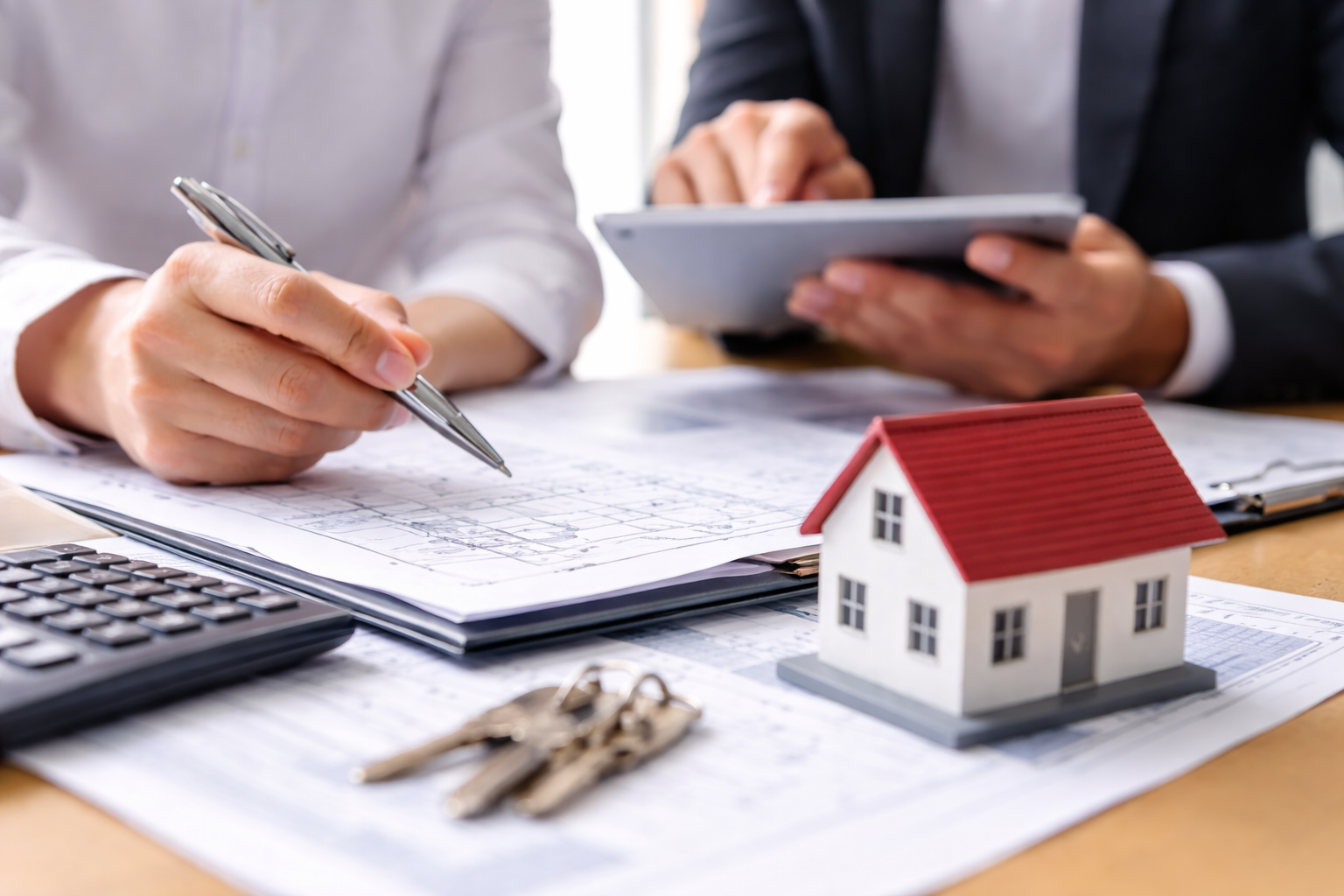 Beratungsgespräch mit Bauplänen, Taschenrechner und Hausmodell als Symbol für steuerliche Beratung von Immobilienunternehmen durch die Dr. Hollmann Steuerberatungsgesellschaft mbH.