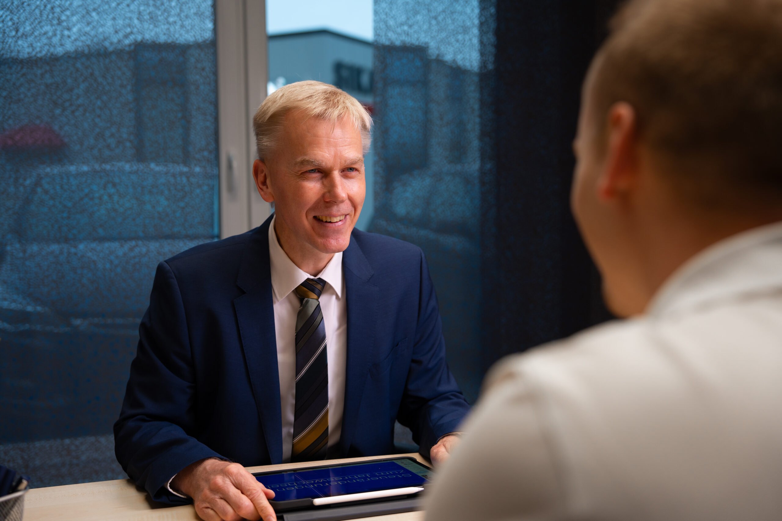 Steuerberater im persönlichen Beratungsgespräch mit Mandant am Tisch, Nutzung eines Tablets zur Analyse von Finanzdaten.
