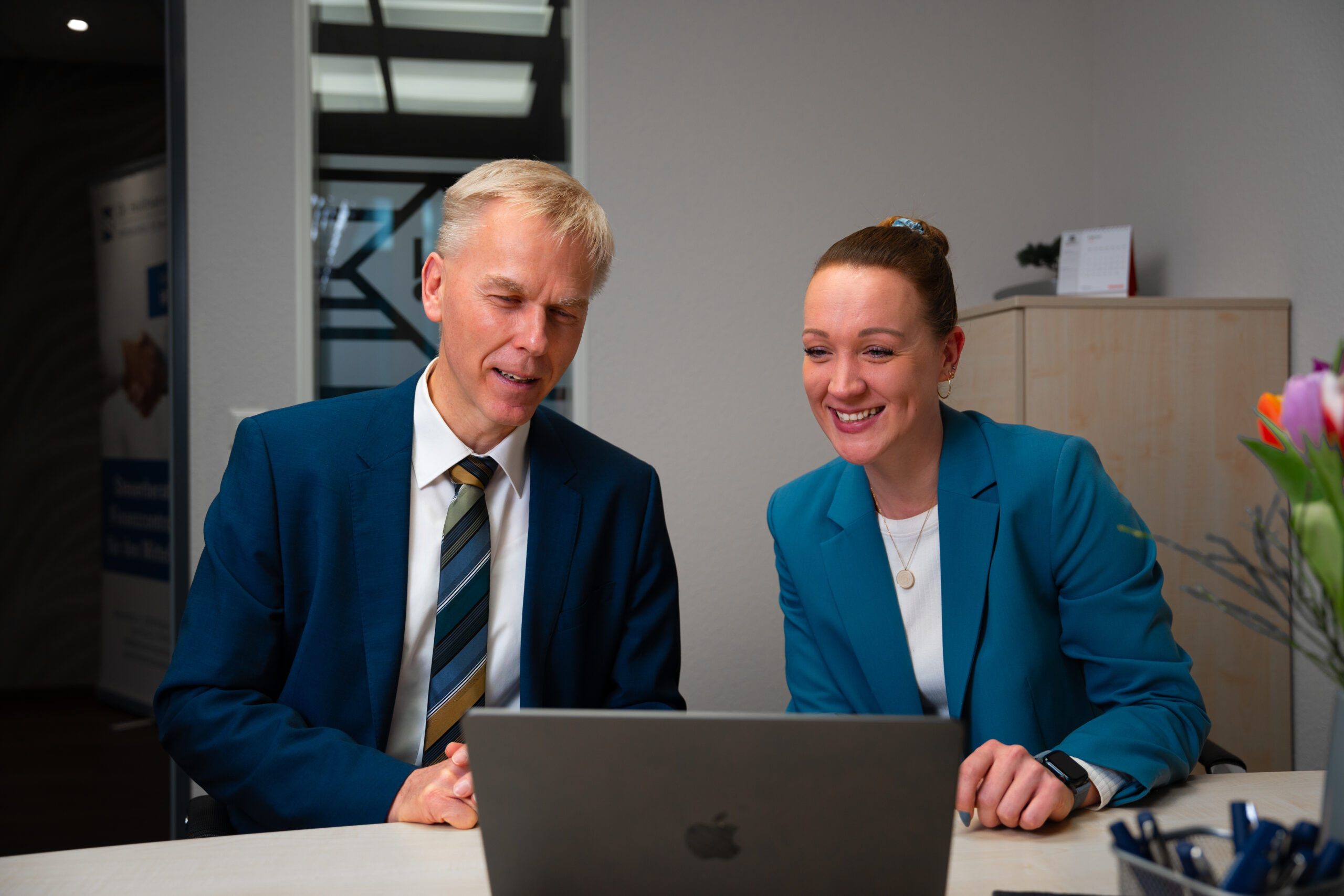 Steuerberater Sebastian Hollmann und Mitarbeiterin analysieren gemeinsam Unternehmenszahlen am Laptop in der Kanzlei in Rheda-Wiedenbrück.